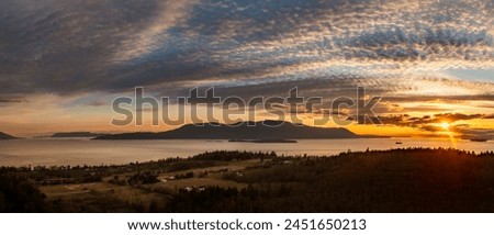 Panoramic sunset aerial view of Orcas Island seen from Lummi Island, Washington. Looking across Rosario Strait towards the San Juan Islands with a dramatic sunset sky over Orcas Island. Royalty-Free Stock Photo #2451650213
