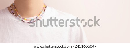 Banner with flower beads on a woman in a white t-shirt in front of beige background. Handmade accessory concept with copy space.
