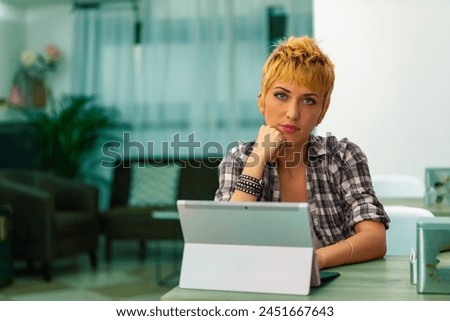 in a modern interior, a woman contemplates her next move, tablet-laptop poised for action Royalty-Free Stock Photo #2451667643