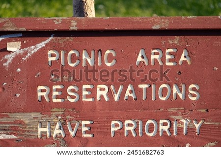 A weathered wooden sign with carved lettering that reads "PICNIC AREA RESERVATIONS HAVE PRIORITY"
