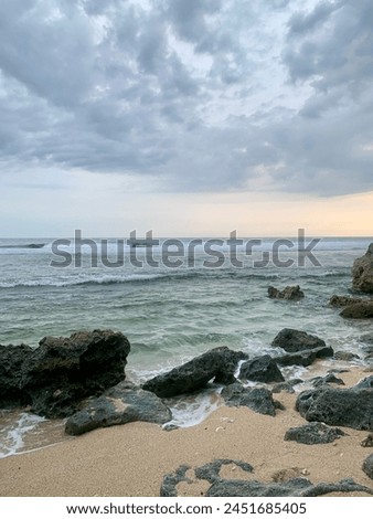photo of a beach with waves on coral rocks. covered in brown sand. contrast to the blue sky and white clouds.