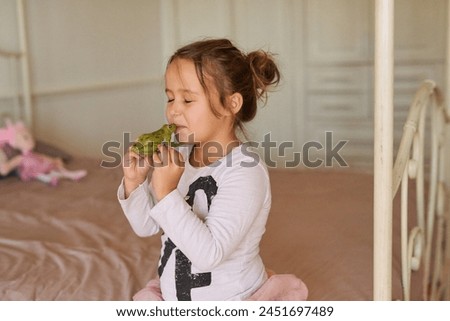 Child, toy and girl kissing frog in bedroom for fairytale, happiness or playing in family home. Kiss, pretend and young kid on bed with object in playroom for having fun, playful or game in apartment