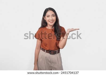 Happy Asian woman is smiling and pointing to the copy space beside her over isolated white background.