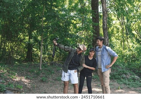 Group of three Asian friends, two men and one woman, have a good relationship, hiking in the forest adventure and holding a camera to take pictures together in summer time trip on holiday.