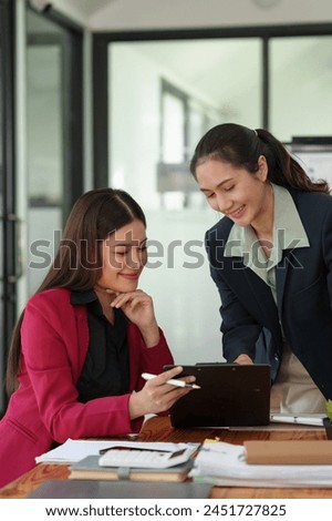 Two Asian businesswomen talk, consult, and discuss work with the presentation of project ideas, growth analysis, marketing and investment plans, and data from charts in an organization in the office.