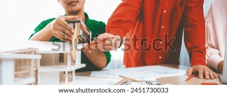 Smart interior designer compares color between color swatches and house model on meeting table with house model and architectural document scatter around. Creative working concept. Variegated