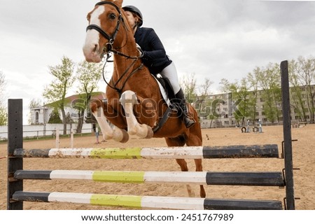 Equestrian event, rider and horse mid-obstacle course. Female jockey in uniform. Show jumping. Horseback riding school Royalty-Free Stock Photo #2451767989