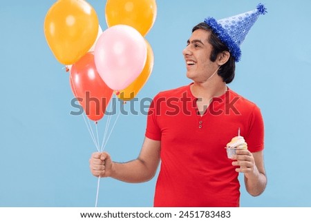 Portrait of cheerful boy in birthday hat standing with balloons and cake
