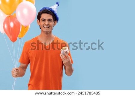 Portrait of cheerful boy in birthday hat standing with balloons and cake