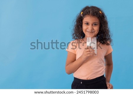PORTRAIT OF A HAPPY GIRL LOOKING AT CAMERA WHILE DRINKING MILK
 Royalty-Free Stock Photo #2451798003