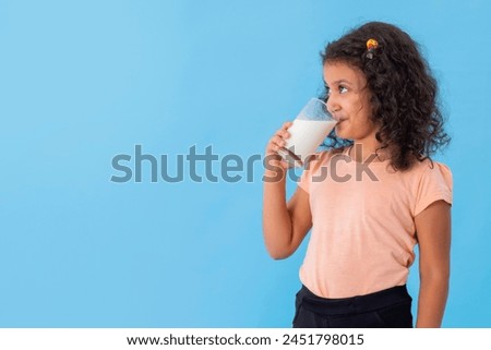 A GIRL CHEERFULLY DRINKING A GLASS OF MILK
