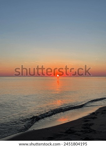 The gentle shades of the orange sun reflecting on the calm waters of the Baltic Sea during sunset create a magical and peaceful atmosphere.