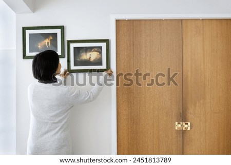 Woman hanging picture frames on a white wall at home. Fairytale glowing mushroom photos in the frames. 