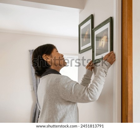 Woman hanging pictures on a wall at home. Fairytale glowing mushroom photos in the frames. 