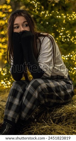 Beautiful young female model sitting on the street on the street in city environment surrounded with decorative lights during nighttime.