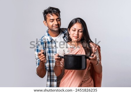 portrait of smiling Indian asian young couple with wooden and metal kitchen utensils, standing isolated on white