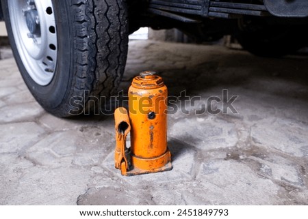 An orange jack with car tires in the background, stock photo.