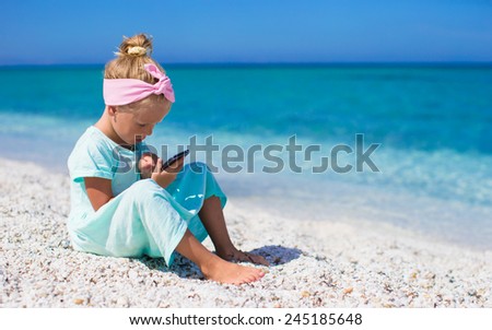 Little cute girl taking pictures on phone at tropical beach