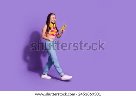 Photo of adorable positive cute girl wear trendy clothes walk empty space isolated on purple color background