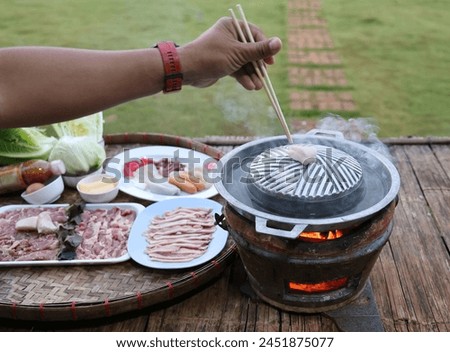 Use chopsticks to pick up the pork pieces and place them on the preheated grill pan. Thai style barbecue grill Hot pan pork buffet Traditional Thai style BBQ Trays of other meat were placed next.  Royalty-Free Stock Photo #2451875077
