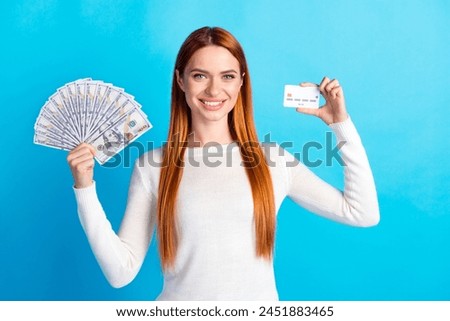 Photo portrait of attractive young woman hold money fan credit card dressed stylish white clothes isolated on blue color background