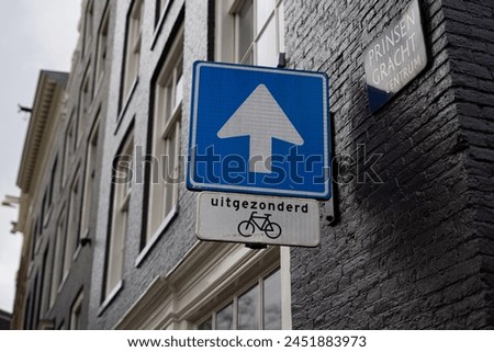 Blue square sign white arrow pointing directing forward car vehicle traffic smaller black text bike bicycle symbol Dutch word “uitgezonderd” means “except” “except bikes” signal caution street name