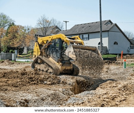 Small bulldozer filling in a drainage trench with loose stone as part of a new housing development infrastructure Royalty-Free Stock Photo #2451885327