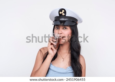 An attractive young Asian woman in a baby blue dress and captain's hat enjoys a refreshing iced tea. Ideal for party cruise themes, isolated on a white background.