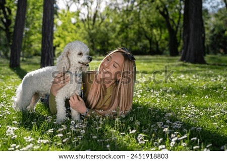 Cute blonde girl laying on the grass with her pet poodle , spring time