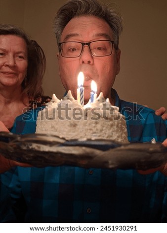 A man about to blow out the candles on his cake with his wife beside him