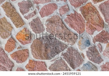 It's close up view of the colorful wall. Its photo of multicolor stonewall. It is photo of multicolored srone wall. its view of red sidewalk. It's view of mosaic color stones