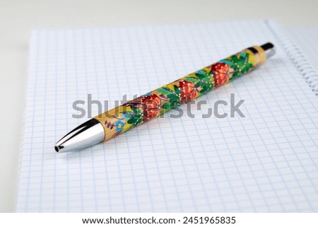 Spiral-bound notebook with a pen resting on top. Petrykivka hand made painting. Ukrainian art tradition.