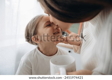 A tender moment between a mother and happy little daughter, with the mother kissing her smiling child on the cheek.