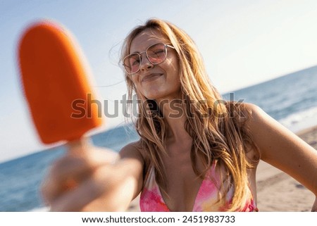 Shot of attractive young woman in bikini eating a orange popsicle looking at the camera on summer