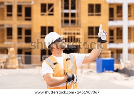 roofer builder working on roog structure of building on construction site. handsome young male builder in hard hat smiling at camera. Construction Worker on Duty. Contractor and the Wooden House Frame Royalty-Free Stock Photo #2451989067