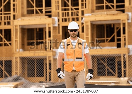 roofer builder working on roog structure of building on construction site. handsome young male builder in hard hat smiling at camera. Construction Worker on Duty. Contractor and the Wooden House Frame Royalty-Free Stock Photo #2451989087