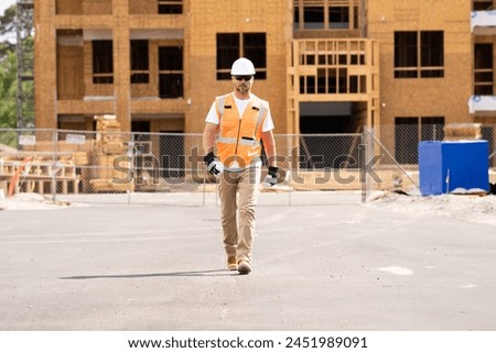 roofer builder working on roog structure of building on construction site. handsome young male builder in hard hat smiling at camera. Construction Worker on Duty. Contractor and the Wooden House Frame Royalty-Free Stock Photo #2451989091