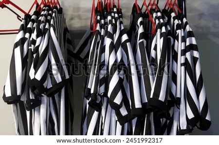 Clothes rack full of referee shirts in different sizes. Black and white uniform and whistle. Basketball ref.