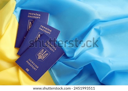 Three Ukrainian biometrical passports on folded waving flag of Ukraine country close up