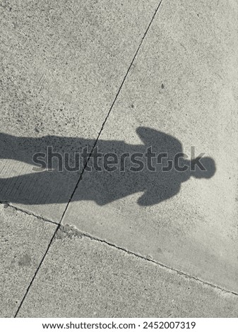 A figure stands in the middle of the road on a bright afternoon, casting a long shadow as the sun illuminates the surroundings. The silhouette of the person, with arms at their sides