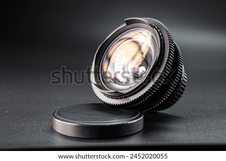 Tilted vintage camera lens on display, colorful light reflection on glass, detailed focus mechanism, photography gear against a dark background