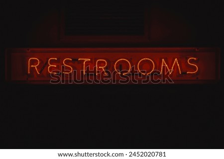 A vibrant red neon sign displaying the word 'RESTROOMS' mounted on a dark wall, emitting a soft glowing light in a dimly lit ambiance.