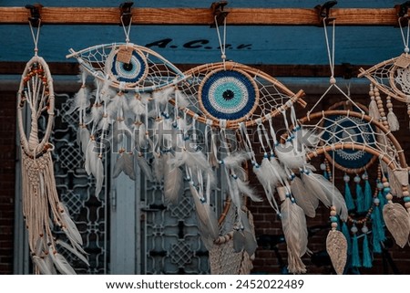 Assorted dream catchers with vibrant eye patterns and feathers hanging at a marketplace. These handicrafts symbolize spiritual traditions and artistic expressions. Royalty-Free Stock Photo #2452022489
