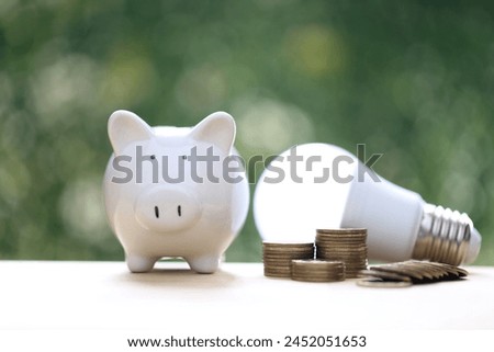 Piggy bank and stack of coins money with light bulb on natural green background,Saving money and energy saving concept