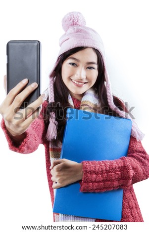 Portrait of teenage student in winter clothes taking self photo with a mobile phone, isolated on white