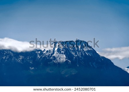 Looking up famous Stanserhorn mountain with restaurant on top with rock and snow covered mountains seen from cruise ship on a sunny spring day. Photo taken April 11th, Lake Lucerne, Switzerland.