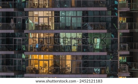 Rows of glowing windows and balconies with people in the interior of apartment building at night. Modern skyscraper with glass surface. Concept for business and modern life