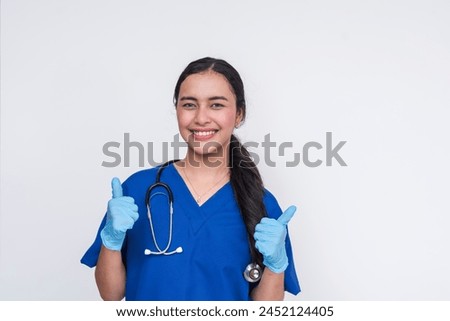 Confident and cheerful Asian female nurse in blue scrubs, giving a thumbs up. Perfect for healthcare and positive medical service imagery.