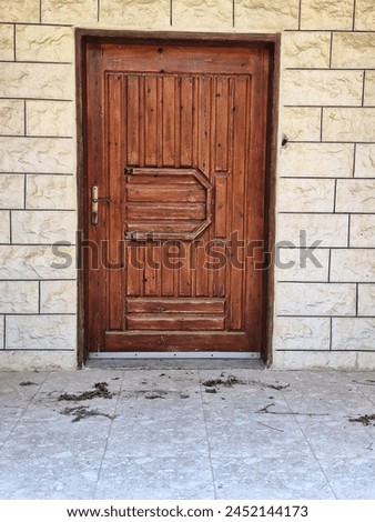 Tall wooden door, geometric design, metal accents, beige stone wall, tiled ground, no signage.
