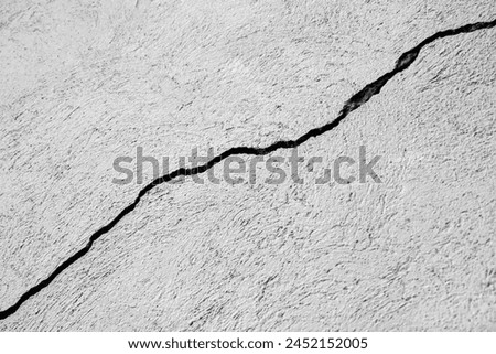 Big winding ascending crack on old gray plastering wall. Thin crack diagonally. Copy space.  Black and white photo. Selective focus. Royalty-Free Stock Photo #2452152005